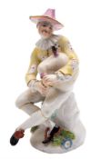A Meissen figure of Harlequin: modelled after Kandler, seated cross legged playing the bagpipes,