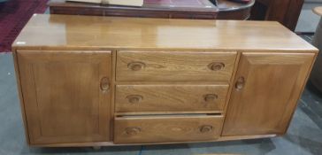 Light elm Ercol sideboard with three central drawers flanked by cupboard doors, the whole raised