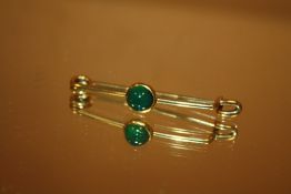 AN UNMARKED YELLOW METAL BAR BROOCH SET WITH POLISHED GREEN STONE