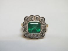 A PRINCESS CUT EMERALD AND DIAMOND RING, the emerald being surrounded by twelve brilliant cut diamon