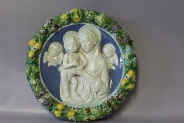 A CIRCULAR MAIOLICA PLAQUE DEPICTING MADONNA AND CHILDREN IN THE STYLE OF DELLA ROBIA, the central