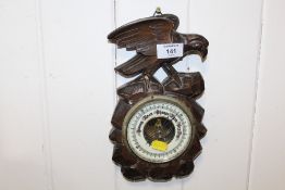 A CARVED BLACK FOREST STYLE BAROMETER WITH BIRD FINIAL TO TOP