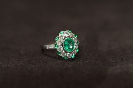 A PLATINUM EMERALD AND DIAMOND DRESS RING, set with a central oval-cut emerald, surrounded by