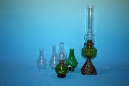 A CAST METAL AND GREEN GLASS OIL LAMP TOGETHER WITH ANOTHER AND ASSORTED LAMP FLUES