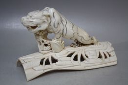 A MEIJI PERIOD CARVED IVORY JAPANESE TIGER ON A PIERCED BRANCH BASE, the tiger with incised stripe