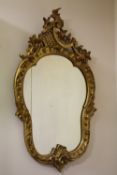 A DECORATIVE GILTWOOD CARVED WALL MIRROR, the shaped glass set within a carved Rococo style frame