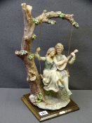 A BELCARI PARIAN FIGURE OF COUPLE ON A SWING on a wooden plinth