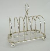 SILVER TOAST RACK on corner bun feet with loop handle and six sections, hallmarked for London