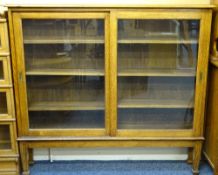 OAK SLIDING DOOR BOOKCASE with interior adjustable shelves and glazed front on tapering supports,