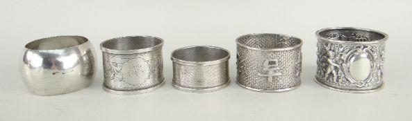 FOUR SILVER NAPKIN RINGS OF VARIOUS DESIGN together with one white metal napkin ring, 118 grams