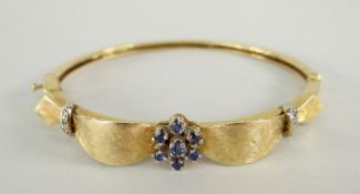 14CT YELLOW GOLD BANGLE with seven-stone sapphire cluster and diamond chip decoration, 17.2grams