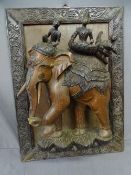 A LARGE BURMESE CARVED ELEPHANT with 3 riding figures on a carved framed panel, 57x78 cms