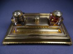 OBLONG BRASS INK STAND on corner supports with centre brass topped blotter and flanking square glass