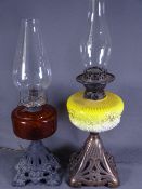 TWO IRON BASED OIL LAMPS, one with a cranberry reservoir and another with a milk glass yellow