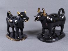 TWO BLACK JACKFIELD COW CREAMERS, one large and the smaller with gilt decoration, each on oval bases