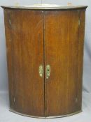 GEORGIAN OAK BOW FRONT HANGING WALL CUPBOARD having twin doors with fancy brass escutcheons and