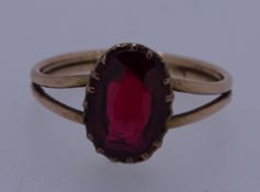 A BELIEVED GOLD (UNMARKED) RING with an oval ruby on split shoulders, 2.5grms, size N/O