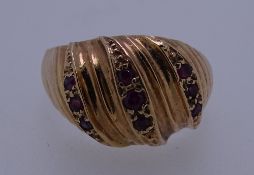 A 9CT GOLD DRESS RING with three rows of tiny rubies in a wavy style setting, 5grms, size O