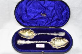 A cased pair of Edwardian silver fruit serving spoons having decorative scrolled rims and gilt