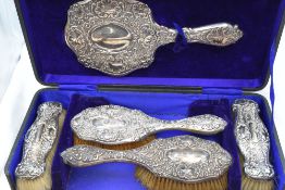 A cased Edwardian silver dressing table set (missing comb) having moulded scroll and flower