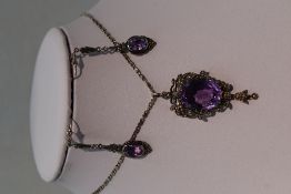 A white metal pendant having large central amethyst style stone within a seed pearl set mount, no