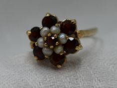 A lady's dress ring having a large garnet and seed pearl daisy cluster on a 9ct gold loop, size