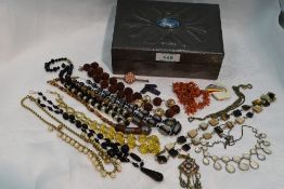 A small pewter backed jewellery box containing a selection of vintage strings of beads including