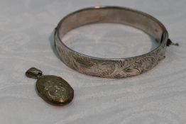 A HM silver hinged bangle having engraved scroll decoration and a small white metal oval locket
