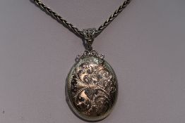 An HM silver locket having engraved scroll decoration on a snake link chain