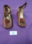 A pair of brown leather baby shoes having pom-pom's to the fronts and strap with button fastening.