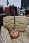 A traditional copper warming pan with brass mounts