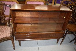 A vintage mahogany display cabinet having sliding glazed door shelf section over two drawers, with