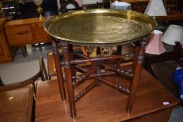 An Eastern brass tray table having turned wood folding frame, diameter approx. 58cm