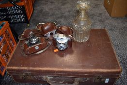 A vintage suitcase containing two cameras and a decanter.