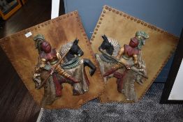Two wooden shield decorative plaques, depicting knights on horseback.