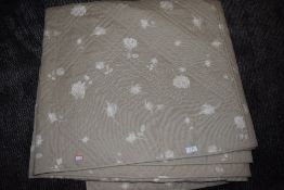 A large modern bed throw having rose print on a beige background.