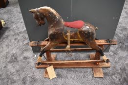 A traditional wooden painted Rocking Horse, missing mane and tail, having fitted saddle, on swing