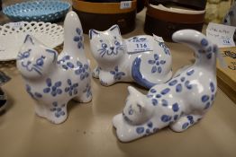 Three blue and white Burnham cat figures in different poses.