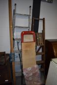 A vintage ironing board and set of aluminium ladders