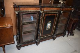 A large empire style ebonised cabinet, having central cupboard with painted enamelled plaque,