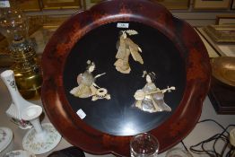 A Lacquered Japanese export wall mounted plaque having mother of pearl Geisha inlay to centre.