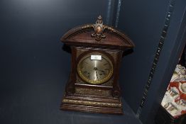 An ornate oak cased mantel clock with bevelled glass face and intricate metal decorations