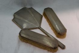 A silver dressing table hand mirror and two clothes brushes all having engine turned decoration,