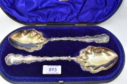 A cased pair of Edwardian silver fruit serving spoons having decorative scrolled rims and gilt