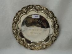 A white metal plate having repousse floral and scroll decoration with central presentation