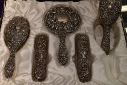 A cased five piece silver dressing table set having embossed mask, bird and scroll decoration,