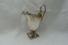 An Edwardian silver cream jug of plain helmet form having reided loop handle and square platform