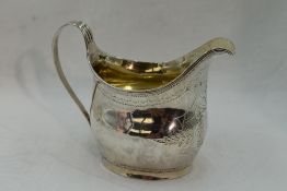 A Georgian silver cream jug of helmet form having engraved and bright cut decoration with crest to