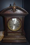 An ornate oak cased mantel clock with bevelled glass face and intricate metal decorations