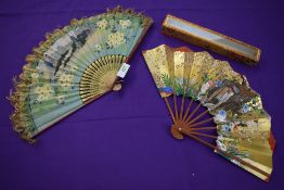 Two oriental hand painted paper fans, one having fringing to edge and both with wooden ribs.